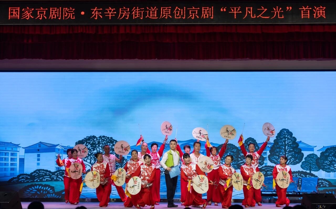 原创京剧《平凡之光》首演：东辛房街道居民与群众文艺队伍登台（台口横幅可辨「国家京剧院·东辛房街道原创京剧《平凡之光》首演」）