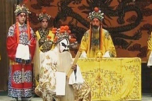 京剧《打金砖》剧照:金殿一场,御案后帝王扮相者(俊扮、黄蟒、黑髯)端坐,白面净角跪陈于前,旁有俊扮角色持笏侍立(央视网《京剧音配像〈打金砖〉》文内所载)