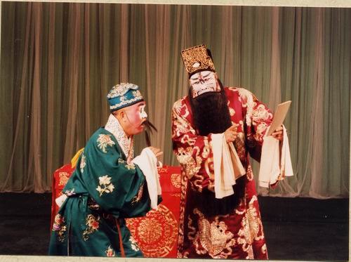京剧《群英会》剧照：丑角与净角对坐，案上置书册（国家京剧院官网剧目页所载）
